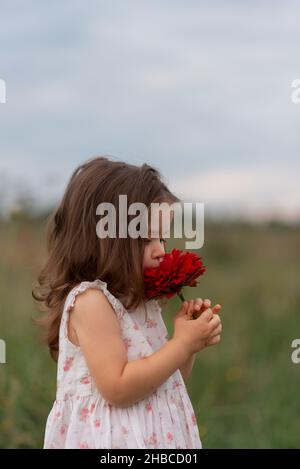 Belle jolie petite fille portant une robe qui sent la grosse fleur rouge. Banque D'Images