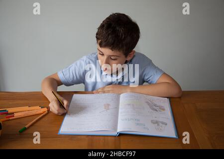 Un garçon d'école, âgé de 11 ans, faisant quelques devoirs avec un livre ouvert contenant des écrits et des dessins Banque D'Images