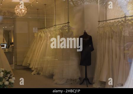 Royaume-Uni.Hiver 2021.Lignes de robes de mariage suspendues sur un rail à travers une fenêtre de magasin de mariage britannique Banque D'Images