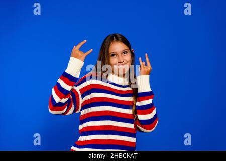 Brunette hispanique fille criant avec l'expression folle faisant le symbole de rock avec les mains vers le haut.Star de la musique.Concept lourd.Isolé sur fond bleu Banque D'Images