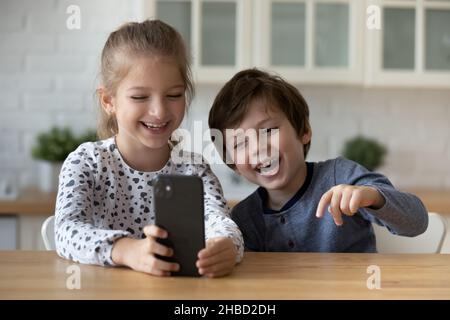 Une petite sœur et un frère débordient de joie à l'aide d'un smartphone, en s'amusant Banque D'Images