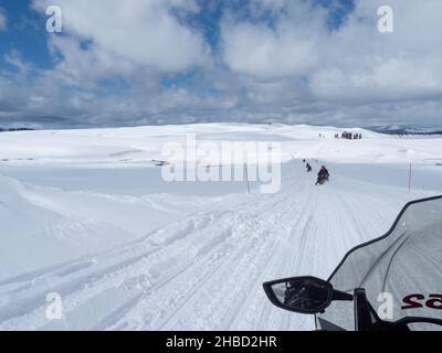 Une excursion en motoneige le long d'une route enneigée dans le parc national de Yellowstone, Wyoming, avec des cumulus au-dessus. Banque D'Images