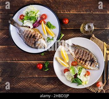 Délicieux dorado grillé ou poisson de mer avec salade, épices, dorada grillé sur une table en bois. Vue de dessus, plan d'appartement, au-dessus de la tête Banque D'Images