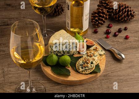 Carte de fête à vin blanc et fromage avec fromage bleu, craquelins et figues sur table en bois, pommes de pin et canneberge Banque D'Images