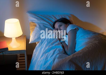 Belle fille souffrant d'insomnie couché dans son lit regardant à travers la fenêtre avec des couleurs bleues de la lune. Banque D'Images