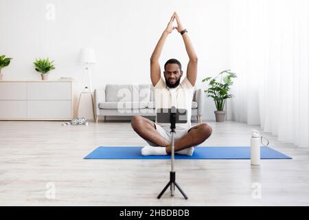 Homme à barbe noire millénaire calme en vêtements de sport blancs, assis sur un tapis en position lotus, pratique le yoga Banque D'Images