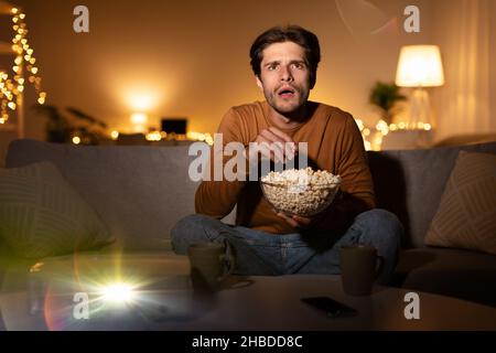 Un homme choqué regardant un film à la maison avec un projecteur de cinéma domestique Banque D'Images