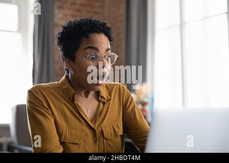 Une jeune femme afro-américaine choquée reçoit des e-mails avec des nouvelles incroyables. Banque D'Images