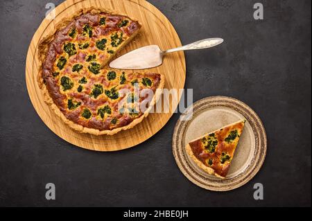 Morceau de tarte sur l'assiette et tarte à la quiche au brocoli et au thon sur une planche à découper ronde en bois avec spatule.Pose à plat Banque D'Images