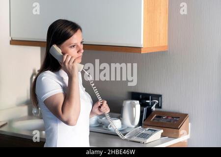 une femme de l'hôtel appelle le personnel de la réception de sa chambre. il y avait probablement une sorte de problème, d'attente et d'anxiété. Banque D'Images