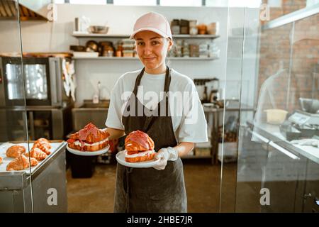 Femme en tablier long contient de délicieux croissants avec remplissage et glaçage dans la boulangerie artisanale Banque D'Images