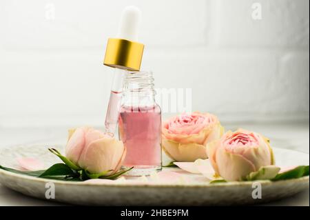 une bouteille ouverte d'huile de rose et une pipette remplie de cosmétiques pour le rajeunissement et le soin du visage sur une plaque en céramique Banque D'Images