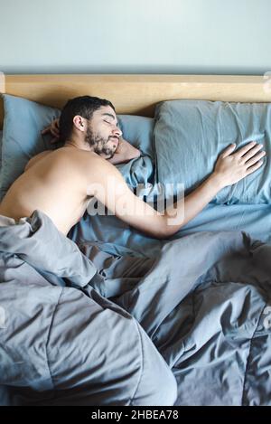 Jeune homme millénial multiracial fin avec barbe dormant à la main sur un oreiller, partenaire manquant, homme simple ou nouvellement célibataire le matin Banque D'Images