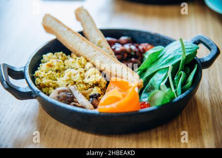 Plat végétarien avec du pain, du riz et des légumes dans une poêle à frire sur une table en bois dans un confortable café végétalien le jour ensoleillé de l'été Banque D'Images