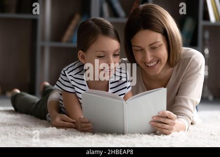 La jeune mère et la fille de la préadolescence se détendent sur la moquette lire le livre Banque D'Images