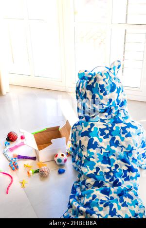 Vue arrière en grand angle d'un enfant méconnaissable dans un pyjama allongé sur le sol avec divers jouets pendant le week-end à la maison Banque D'Images