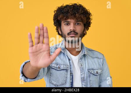 Jeune indien montrant le geste de la main d'arrêt isolé sur fond jaune. Banque D'Images