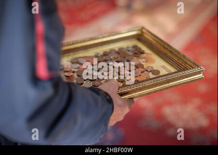 L'homme croyant recueille des dons dans l'église.Les bienfaiteurs mettent de l'argent métallique sur l'icône de la sainte église saint.La coutume chrétienne orthodoxe de l'helpin Banque D'Images