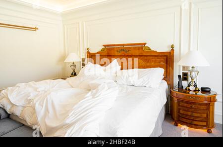 Lit non fait avec literie, draps et draps froissés dans une chambre d'hôtel vide et luxueuse Banque D'Images
