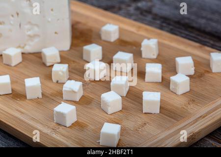 Cubes de fromage feta sur planche à découper en bois.Cubes carrés de fromage feta isolés sur une planche à bois avec couteau. Banque D'Images