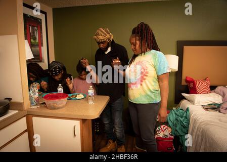 Smyrna, Géorgie, États-Unis.19th décembre 2021.Genetra Quick, son mari handicapé Robert, et trois enfants adolescents vivent de jour en jour dans un hôtel pour séjour prolongé au nord d'Atlanta.La famille est financièrement à court et sans transport pour être en mesure de travailler quand son camion a été repris, parce que le besoin de crédit d'impôt fédéral pour enfants n'a pas pu arriver à temps.Photo : la famille bénit son modeste repas au dîner.Les parents Robert et Genetra s'assurent que leurs filles mangent avant de manger.(Image de crédit : © Robin Rayne/ZUMA Press Wire) Banque D'Images