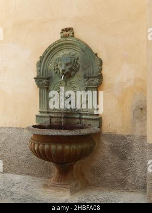 La fontaine à tête de lion dans la rue sur un vieux mur orange Banque D'Images