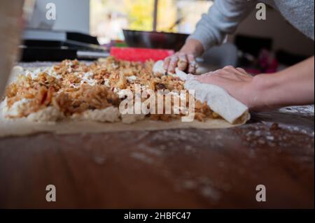 Vue en gros plan des mains de femmes qui roulent la pâte à pâtisserie aux pommes dans une tarte au strudel douce sur la table à manger. Banque D'Images