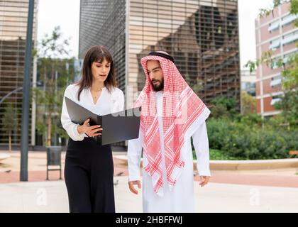 Jeune femme d'affaires europienne serioius expliquant les détails du contrat à un client homme arabe, une femme propriétaire montrant le point de signature dans le contrat de prêt à l'homme d'affaires saoudien lors d'une réunion en plein air Banque D'Images