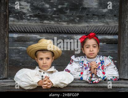 Salaj, Roumanie-15 mai 2018 : enfants portant des costumes roumains traditionnels devant une ancienne église en bois dans la région de Transylvanie, Roumanie. Banque D'Images