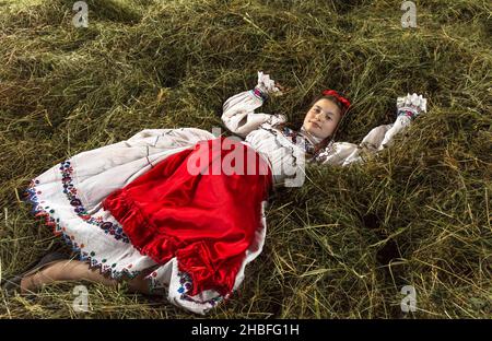 Salaj, Roumanie - 15 mai 2018 : jeune fille rurale vêtue de costumes traditionnels assis dans un hanyloft au moment de la récolte à la campagne Banque D'Images