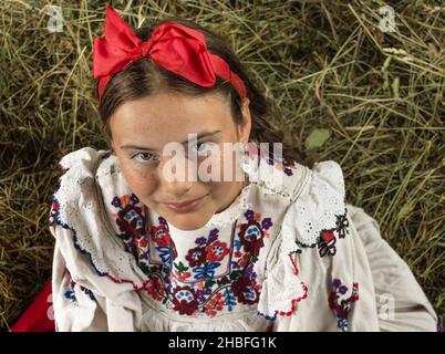 Salaj, Roumanie - 15 mai 2018 : jeune fille rurale vêtue de costumes traditionnels assis dans un hanyloft au moment de la récolte à la campagne Banque D'Images