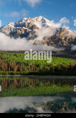 Des nuages peu suspendus tourbillonnent autour de Pyramid Mountain après une dépoussiérage de neige, se reflétant sur le lac Patricia dans le parc national Jasper. Banque D'Images