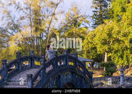 Hilo, Hawaï - 28 novembre 2021 : magnifique parc et jardins de Liliuokalani à Hilo, Hawaï, sur un coucher de soleil pluvieux.Jeune couple prenant des photos. Banque D'Images