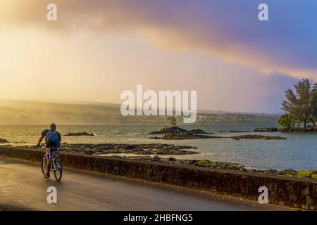 Hilo, Hawaï - 28 novembre 2021 : magnifique parc et jardins de Liliuokalani à Hilo, Hawaï, sur un coucher de soleil pluvieux.Un homme qui fait du vélo sur la route de la plage. Banque D'Images