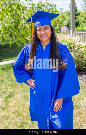 Une belle adolescente avec de longs cheveux foncés dans sa casquette bleue et robe le jour de sa remise des diplômes. Banque D'Images