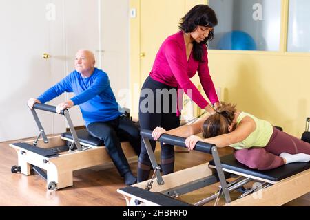 Femme hispanique pilates instructeur aidant la femme s'exerçant sur réformateur Banque D'Images