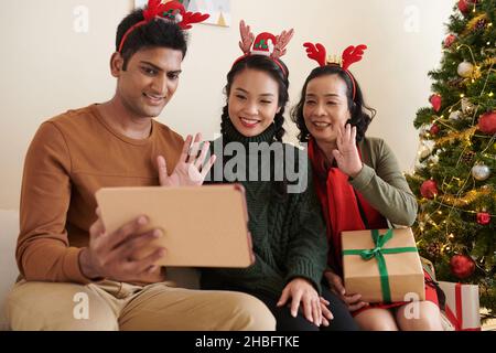 Des membres de la famille souriants agitant avec les mains lorsqu'ils appellent des proches d'une autre ville pour souhaiter un joyeux Noël Banque D'Images