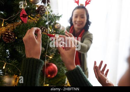 Femme accrochant le jouet sur l'arbre de Noël lors de la décoration de la chambre avec sa mère Banque D'Images