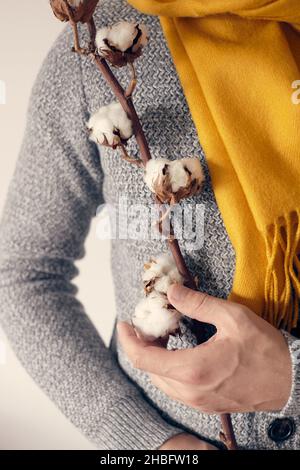 Un homme dans un gilet gris et une écharpe brillante est debout avec une branche de coton sur un fond clair.Vue avant. Banque D'Images