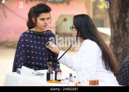 Femme indienne médecin vérifiant le rythme cardiaque de la jeune fille adulte avec stéthoscope à l'extérieur du village, femme faisant l'objet d'un examen par la personne médicale, Rural I Banque D'Images