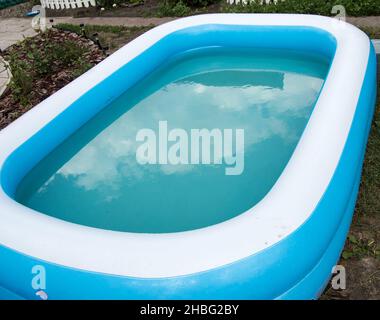 Gros plan d'une piscine gonflable debout sur l'herbe un jour ensoleillé d'été, le reflet des nuages à la surface de l'eau Banque D'Images