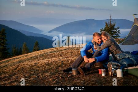 Camping familial dans les montagnes.Bonne femme embrassant son ami souriant près de la tente sur fond de ciel gris d'automne et de montagne brumeuse beskids.Concept de randonnée, de camping et de relations. Banque D'Images