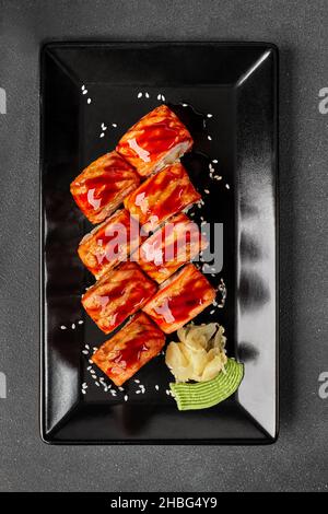 Vue de dessus des petits pains à sushi au saumon flambé avec sauce unagi et sésame sur une assiette noire avec gingembre et wasabi Banque D'Images