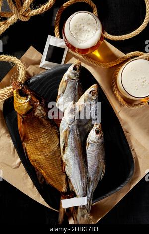 Dorade fumée, cafard séché salé et sabrefrite sur un panneau de bois avec une bière légère mousseuse Banque D'Images