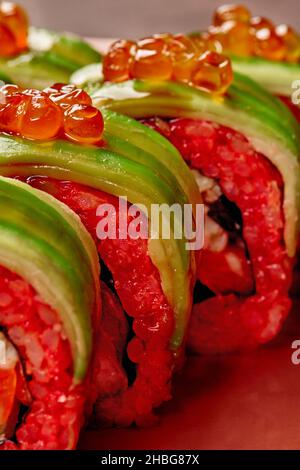 Petits pains à sushis frais et appétissants, farcis avec du saumon cru enveloppés dans de fines tranches d'avocat garni de caviar rouge.Prise de vue macro .Nourriture naturelle Banque D'Images