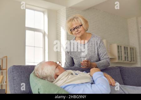 Relation d'un amant.Une femme âgée qui s'occupe donne un verre d'eau à son mari malade de la grippe. Banque D'Images