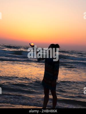 la femme tient le soleil comme il se met dans la paume de sa main Banque D'Images