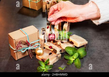 La main de la fille tient une boule d'arbre de Noël rouge sur les morceaux de savon fait à la main à partir d'ingrédients naturels.Cadeaux pour Noël et le nouvel an.Bits Banque D'Images