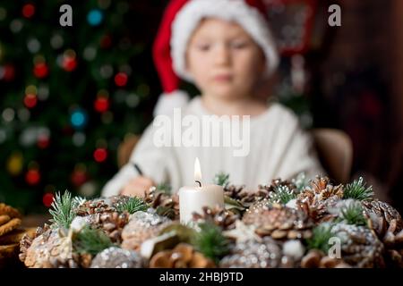 Couronne de l'Avent avec bougie en feu au milieu, enfant écrivant la lettre en arrière-plan, arbre de noël derrière Banque D'Images