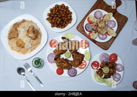 Dose de riz au poulet et de délicieux poulet grillé avec des oignons en tranches et des tomates servis avec la cuillère sur la table blanche Banque D'Images